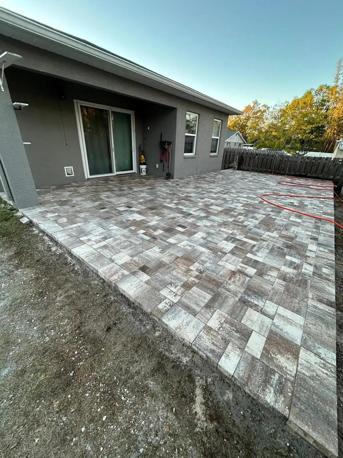 Finished backyard patio in multi-tone concrete pavers running from the sliding door out to the fence.