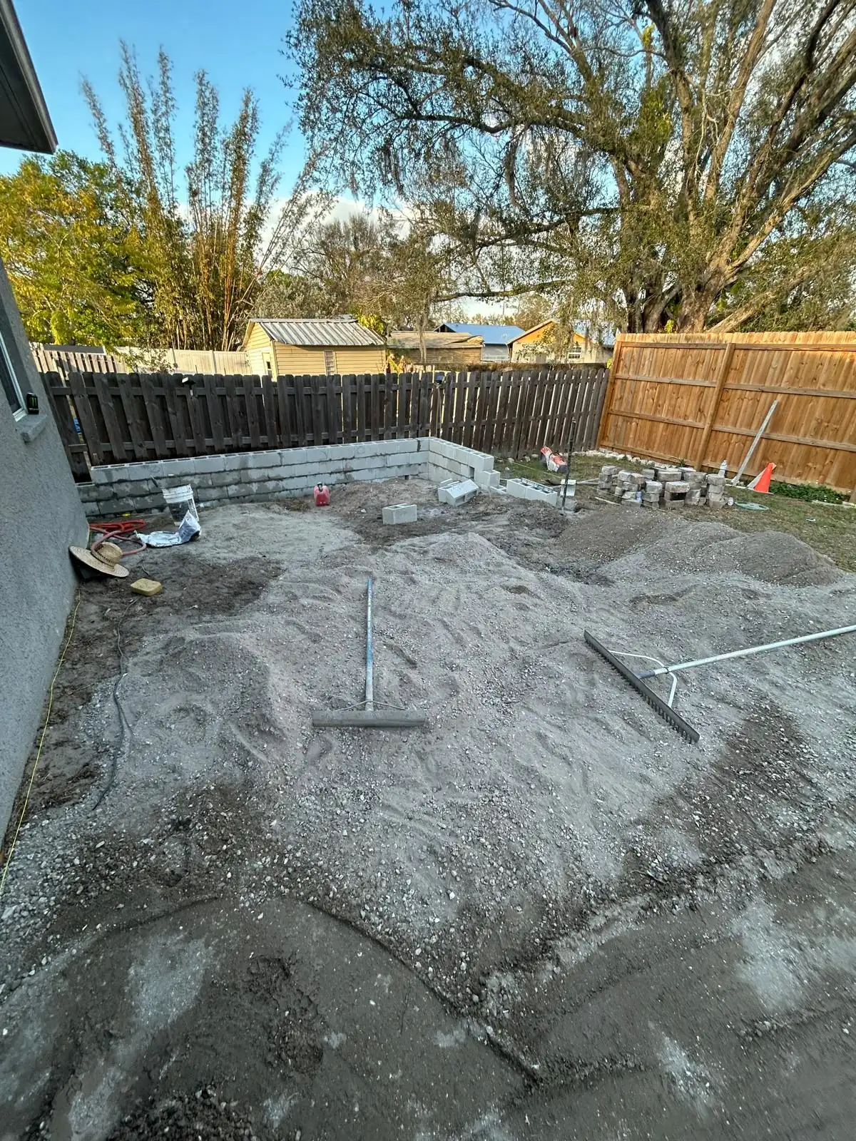 Graded base material raked out across the backyard, with a concrete block border along the back fence.