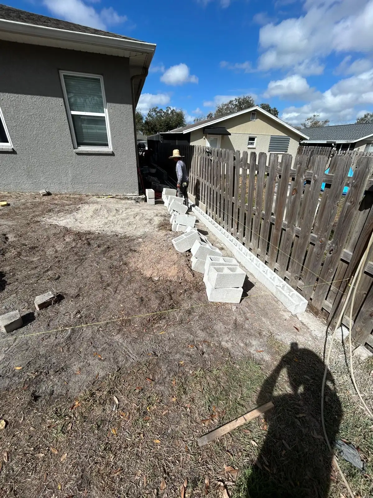 Concrete block edge course going in along the fence line of the bare backyard before the patio base.