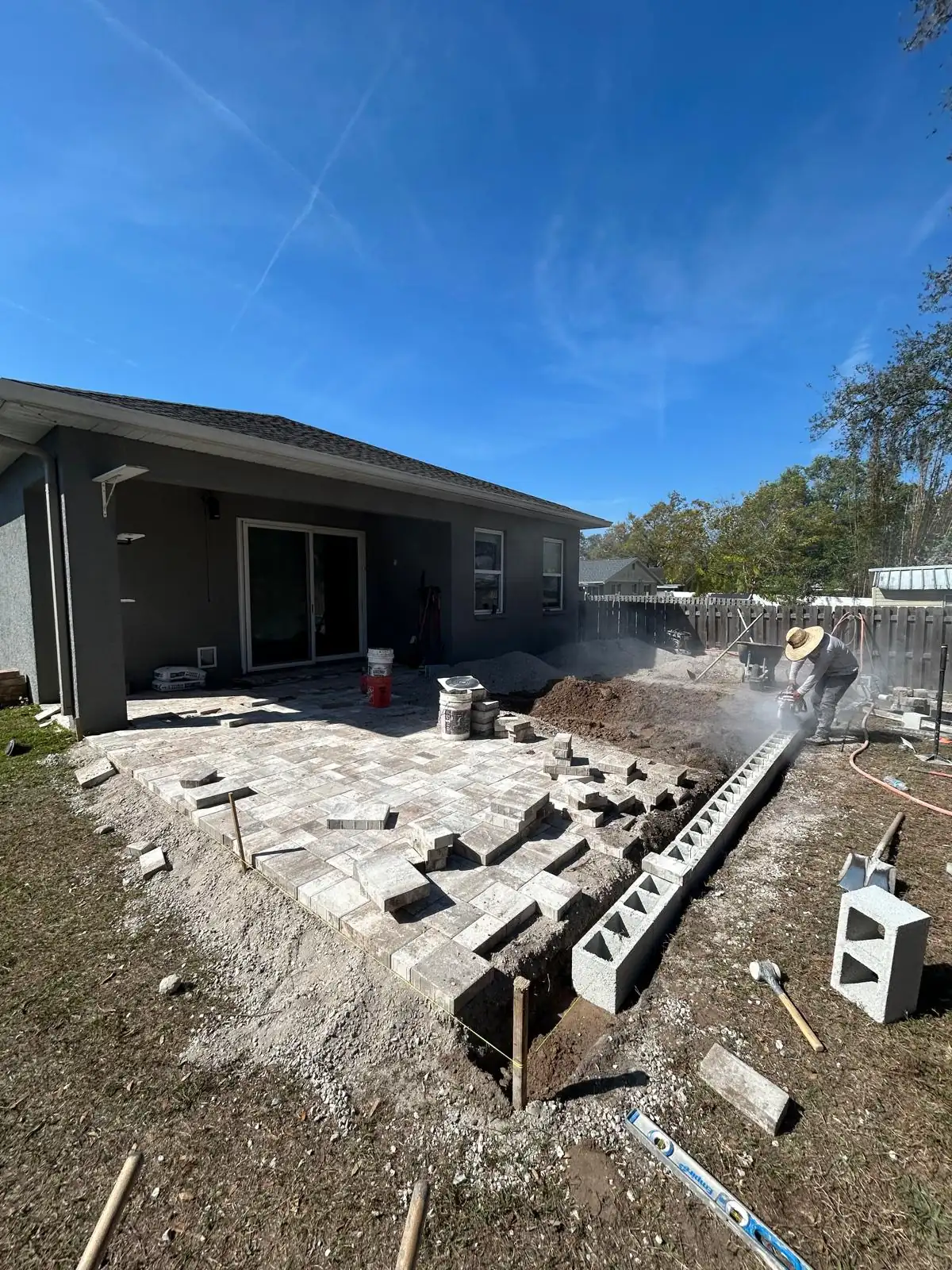 Multi-tone concrete pavers going down over the prepared base while a crew member cuts pieces to fit.