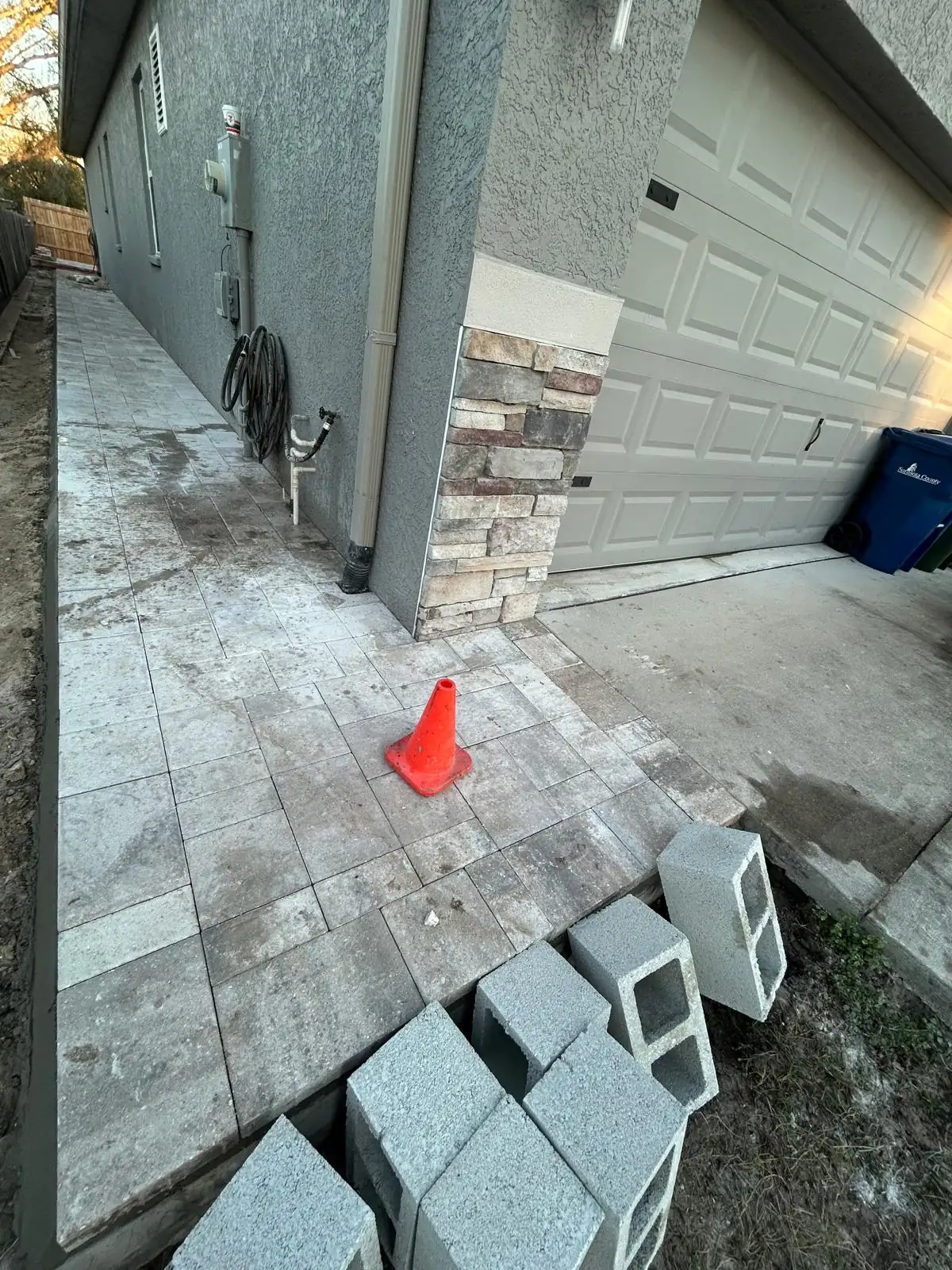 Paver walkway along the side of the house to the garage, with concrete block staged at the edge.