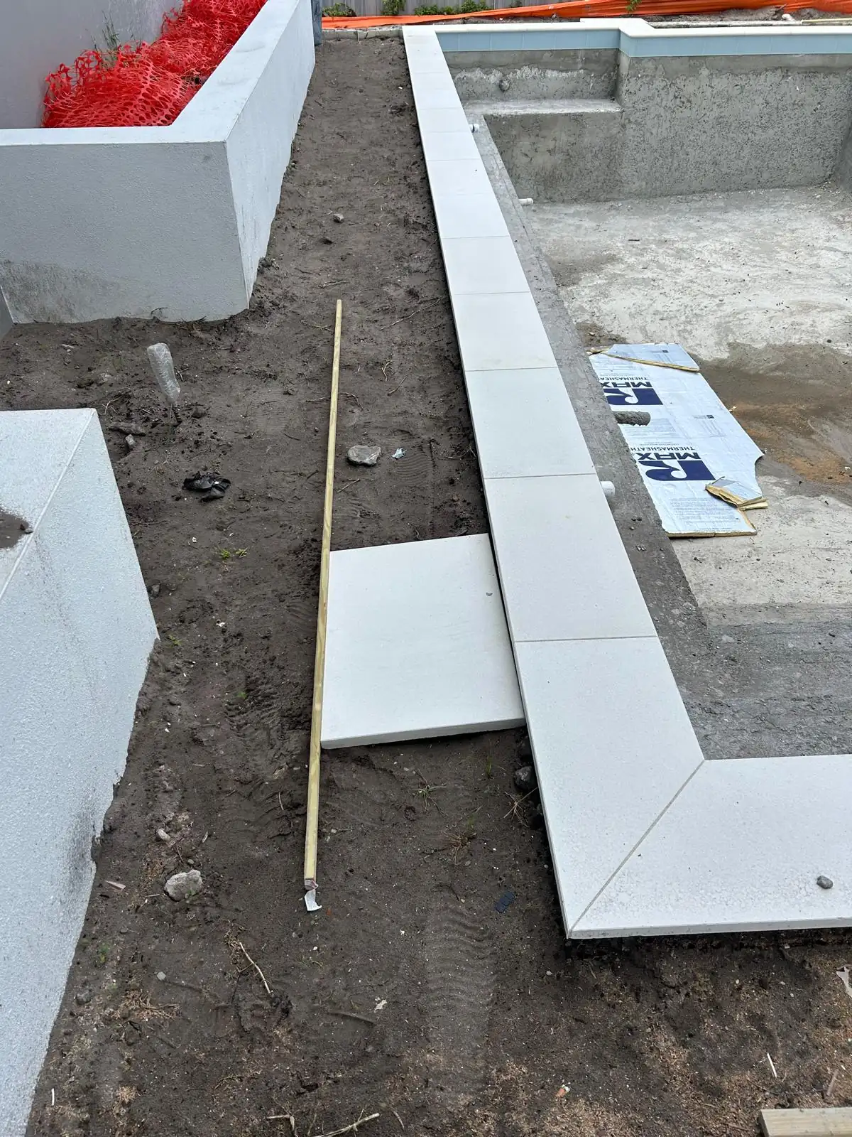 Mitred white stone coping set along the pool edge with a cut piece staged on the bare deck area
