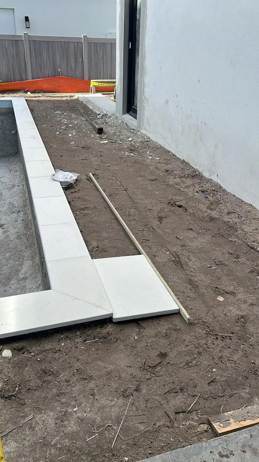 Long run of white stone coping set around the pool edge with the deck area still bare ground