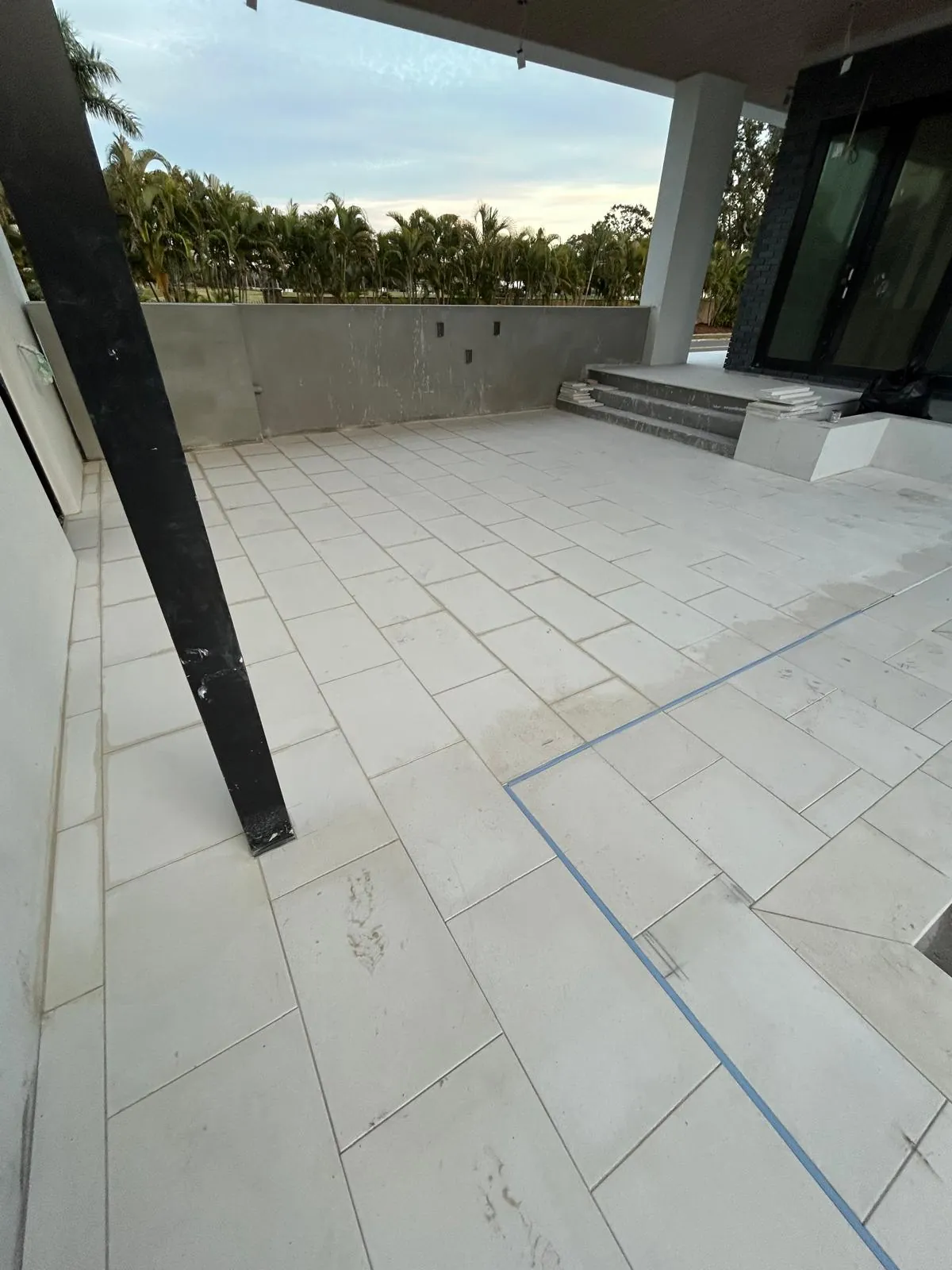 Covered rear patio paved in large format white stone with a blue chalk line snapped across the surface