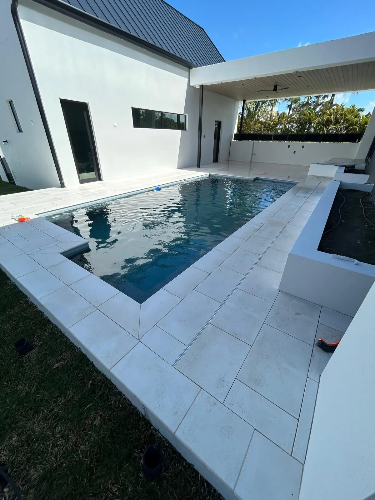 Finished white stone pool deck with mitred coping wrapping a filled rectangular pool at a modern house