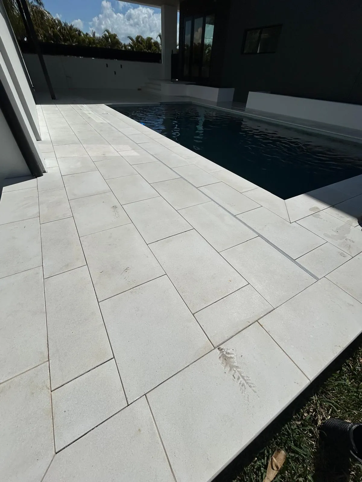 Large-format white stone pool deck running the length of the pool with a linear drain line in the paving