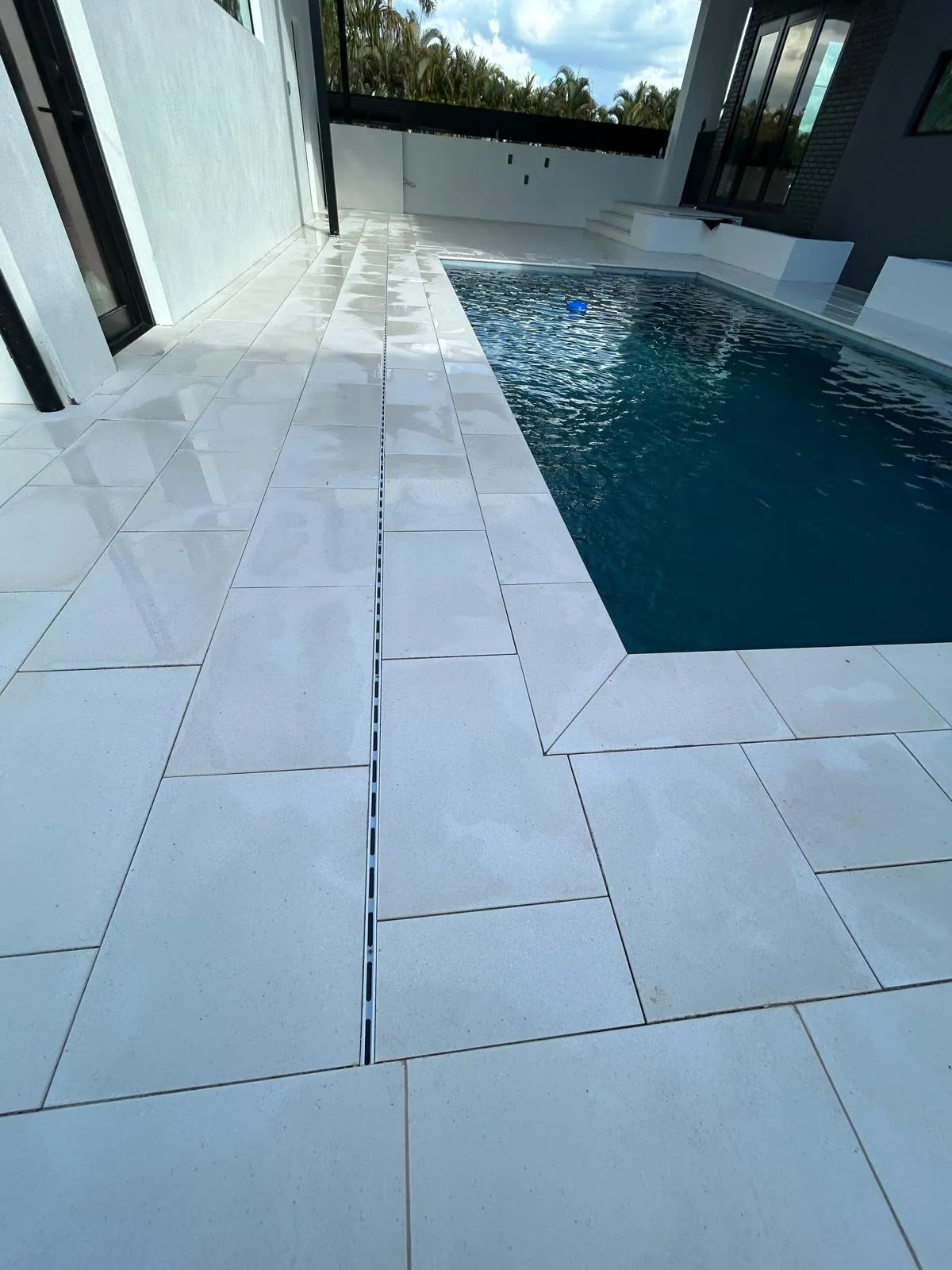 Finished pool deck with a linear drain line and mitred stone coping at the filled pool edge