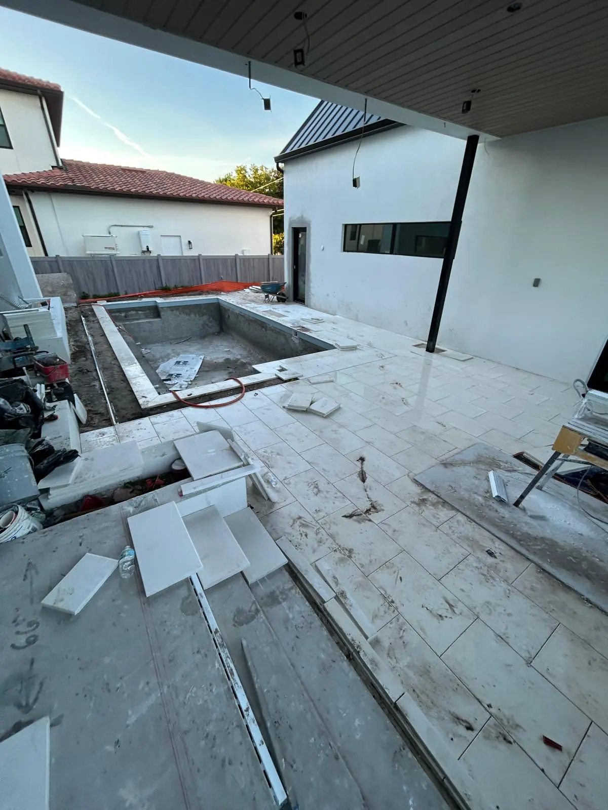 Pool deck part laid in large-format white stone, with cut pieces, a wheelbarrow and levels staged on site