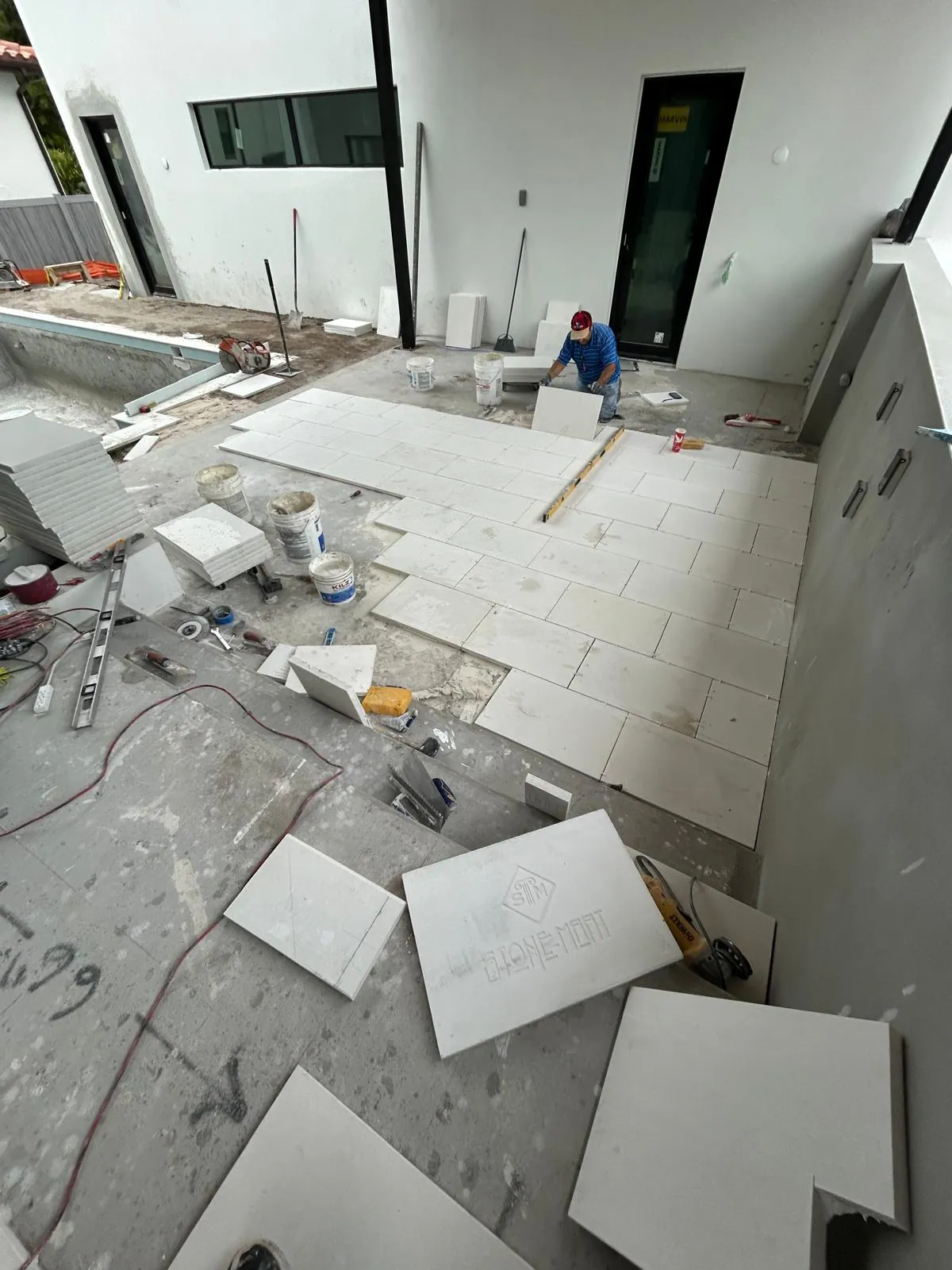 Installer setting a large white stone slab on the deck beside the pool, staged slabs around him