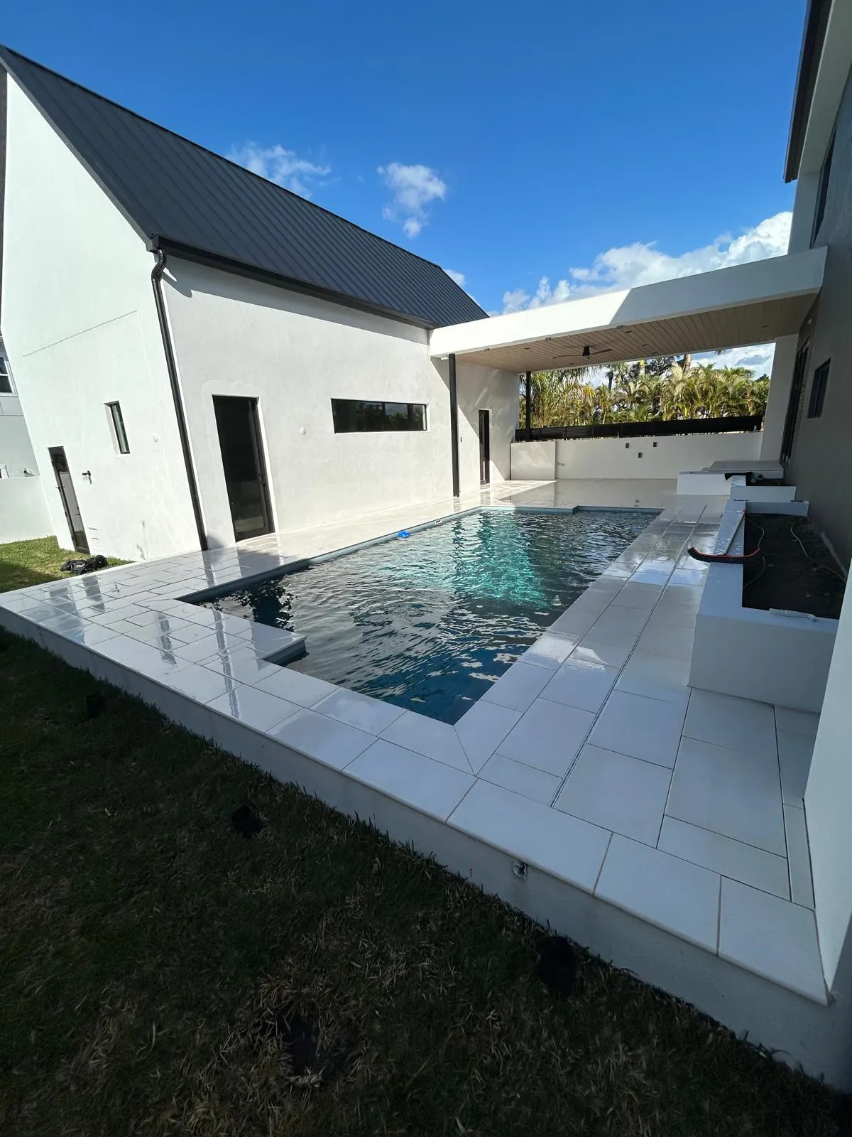 Wide view of the finished white stone pool deck and coping wrapping a filled pool at a modern house