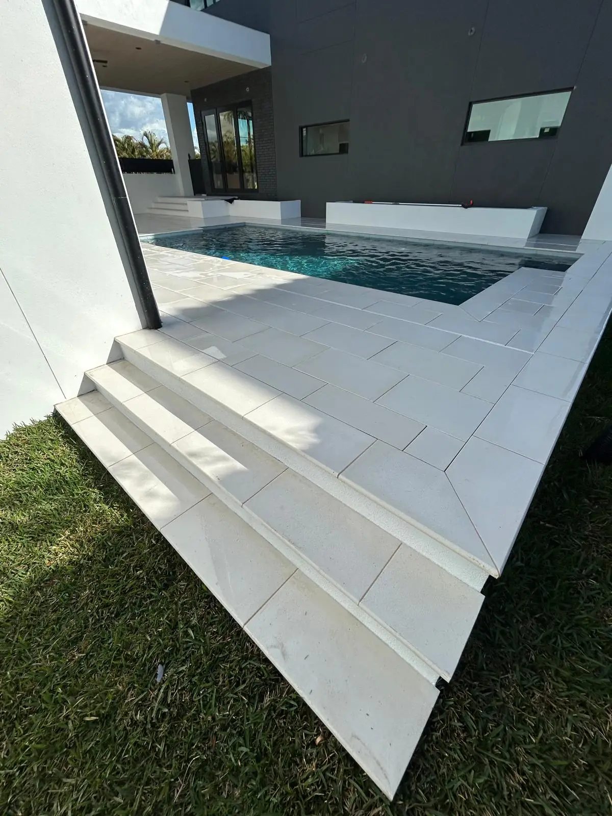 Wide stone steps with bullnose treads lead from the lawn up to the finished pool deck