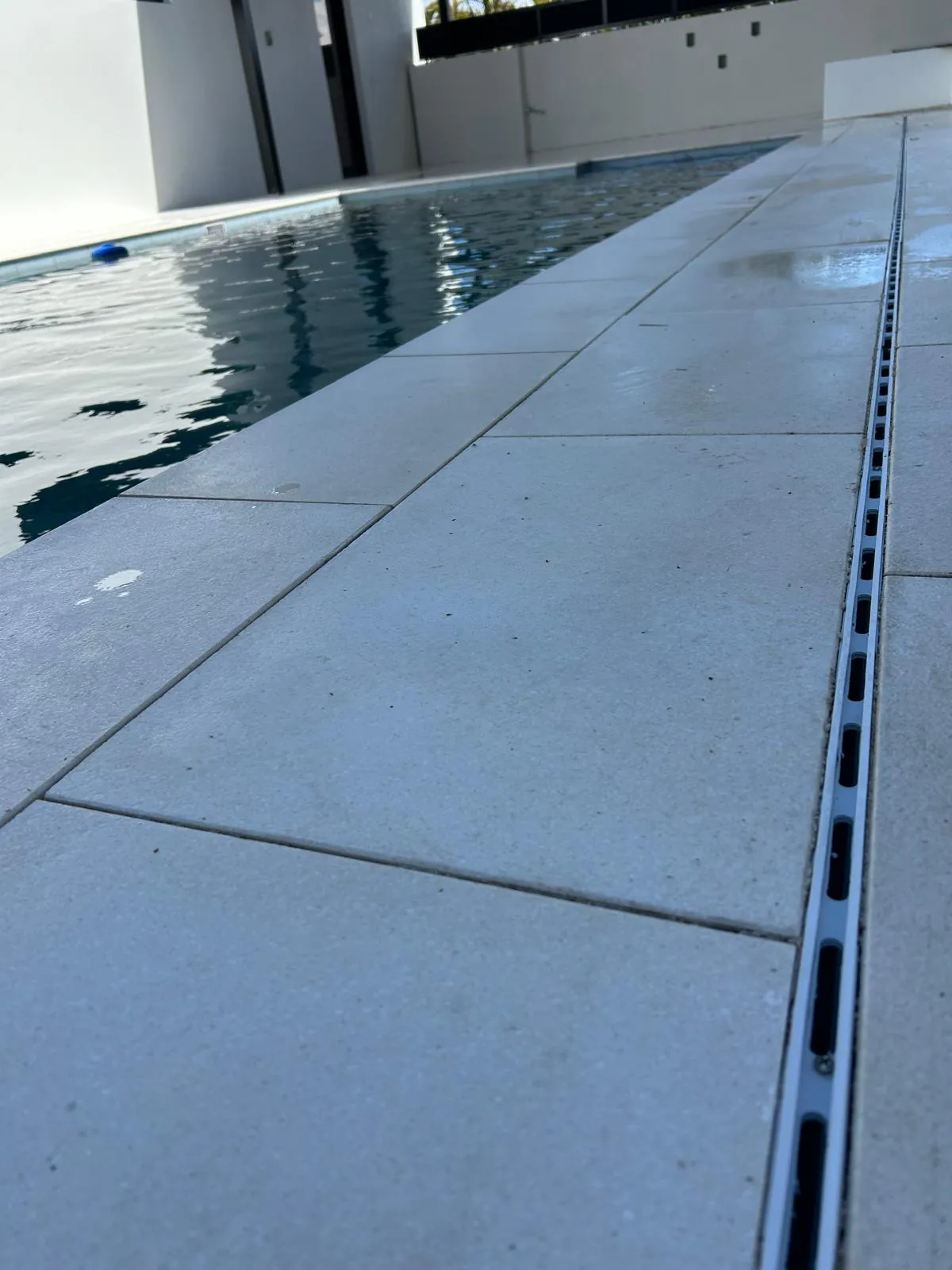 Close view of the pool deck with a slim linear drain set flush in the stone beside the coping