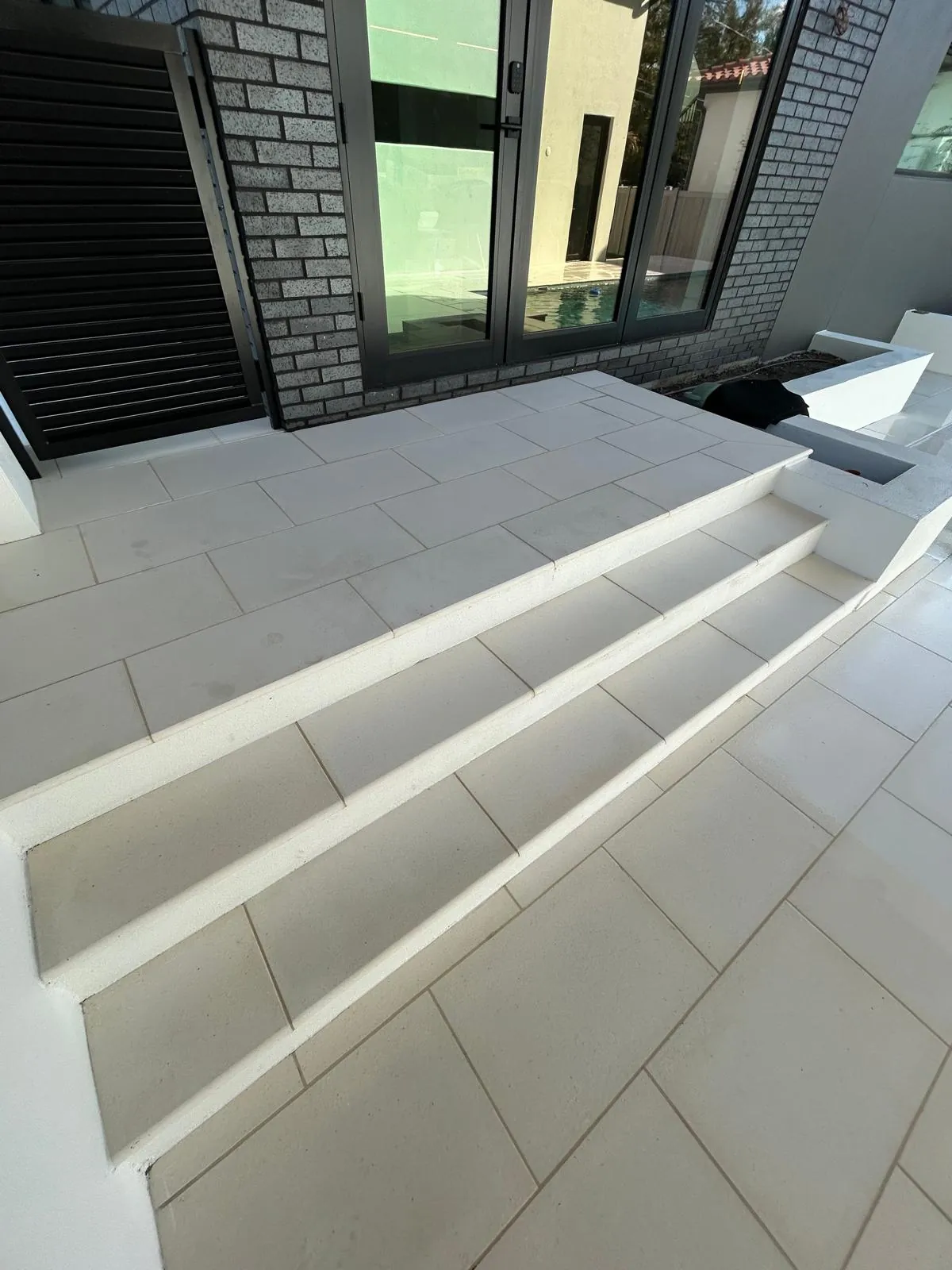 Wide stone steps and a landing in matching stone rise from the pool deck to the rear glass doors