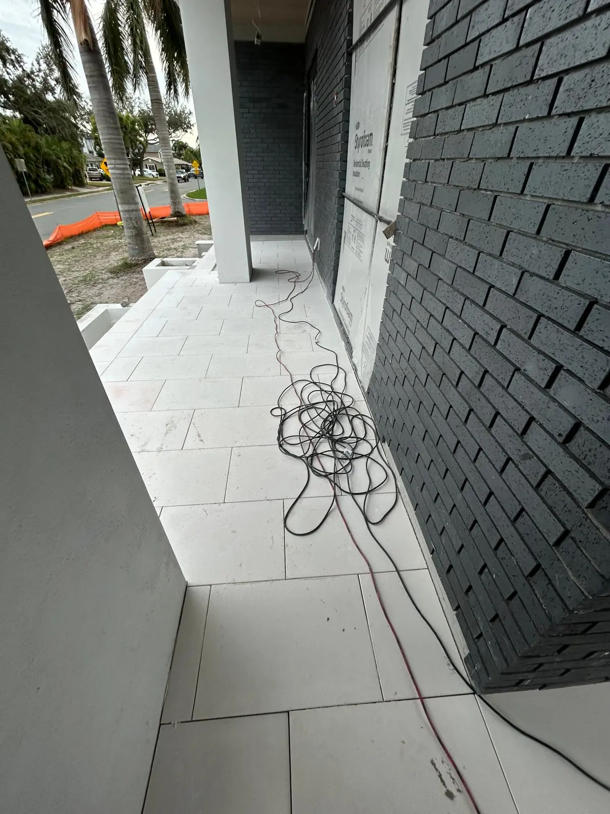 Finished white stone walkway running tight along the dark grey brick wall toward the street