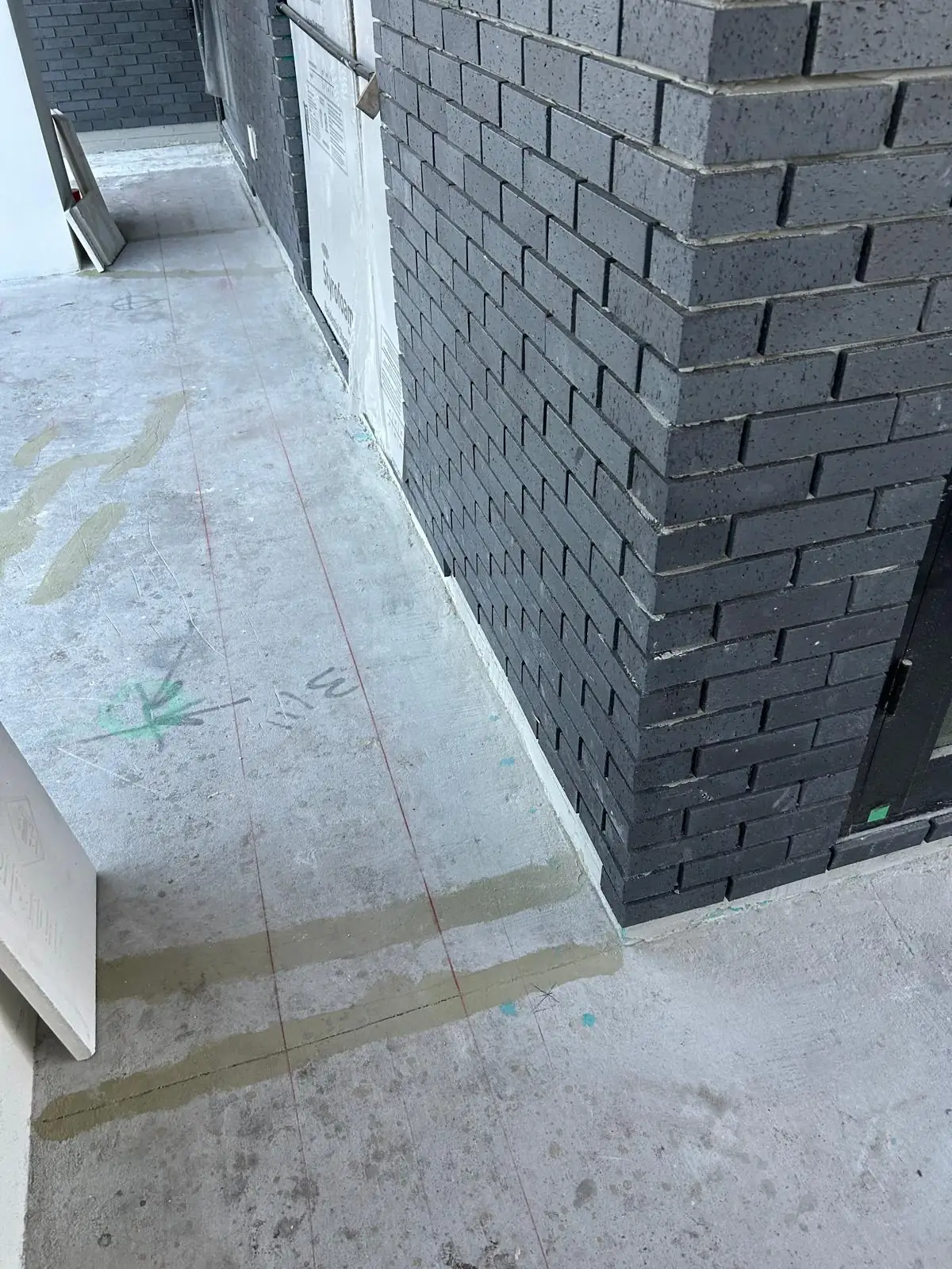 Bare concrete with red layout lines snapped along the dark grey brick wall before stone paving