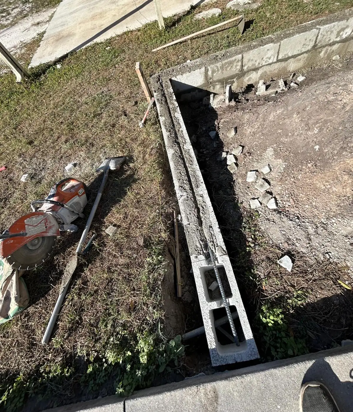 Poured concrete footer running the length of the trench with the first block and rebar set at the near end