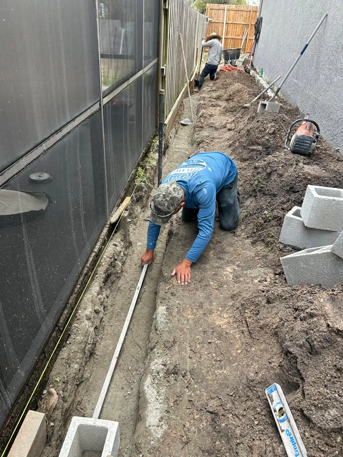 Crew member leveling the bottom of the excavated trench along a string line before block is set